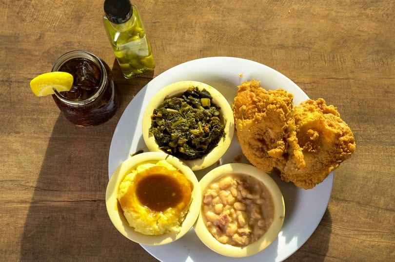 Southern comfort food plate with fried chicken, collard greens, mashed potatoes, beans, and iced tea.